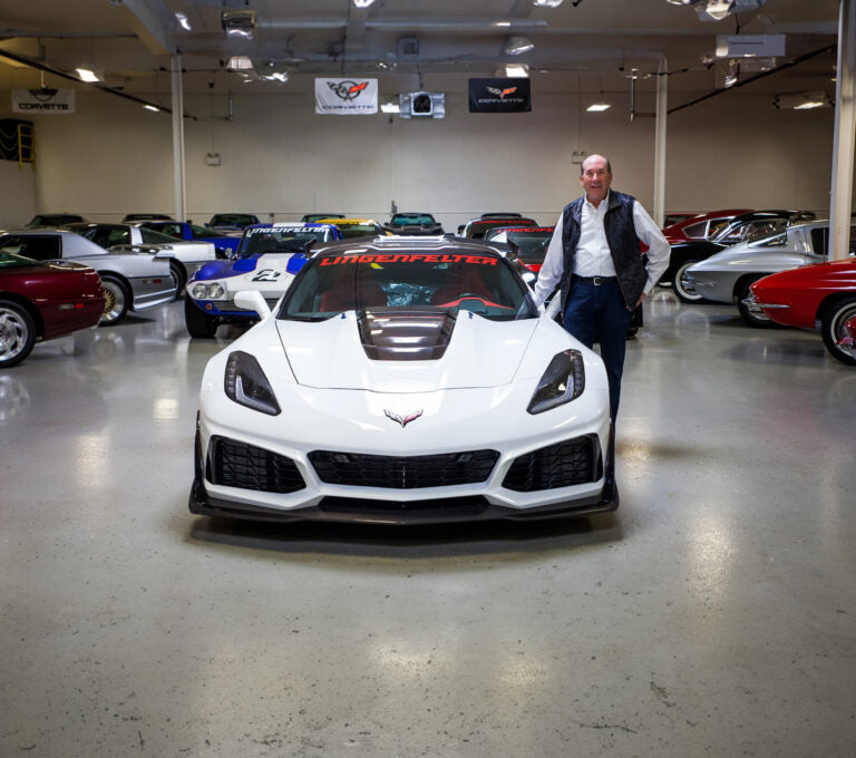 Ken Lingenfelter stands beside a white Corvette ZR1 in a showroom filled with classic Corvettes.