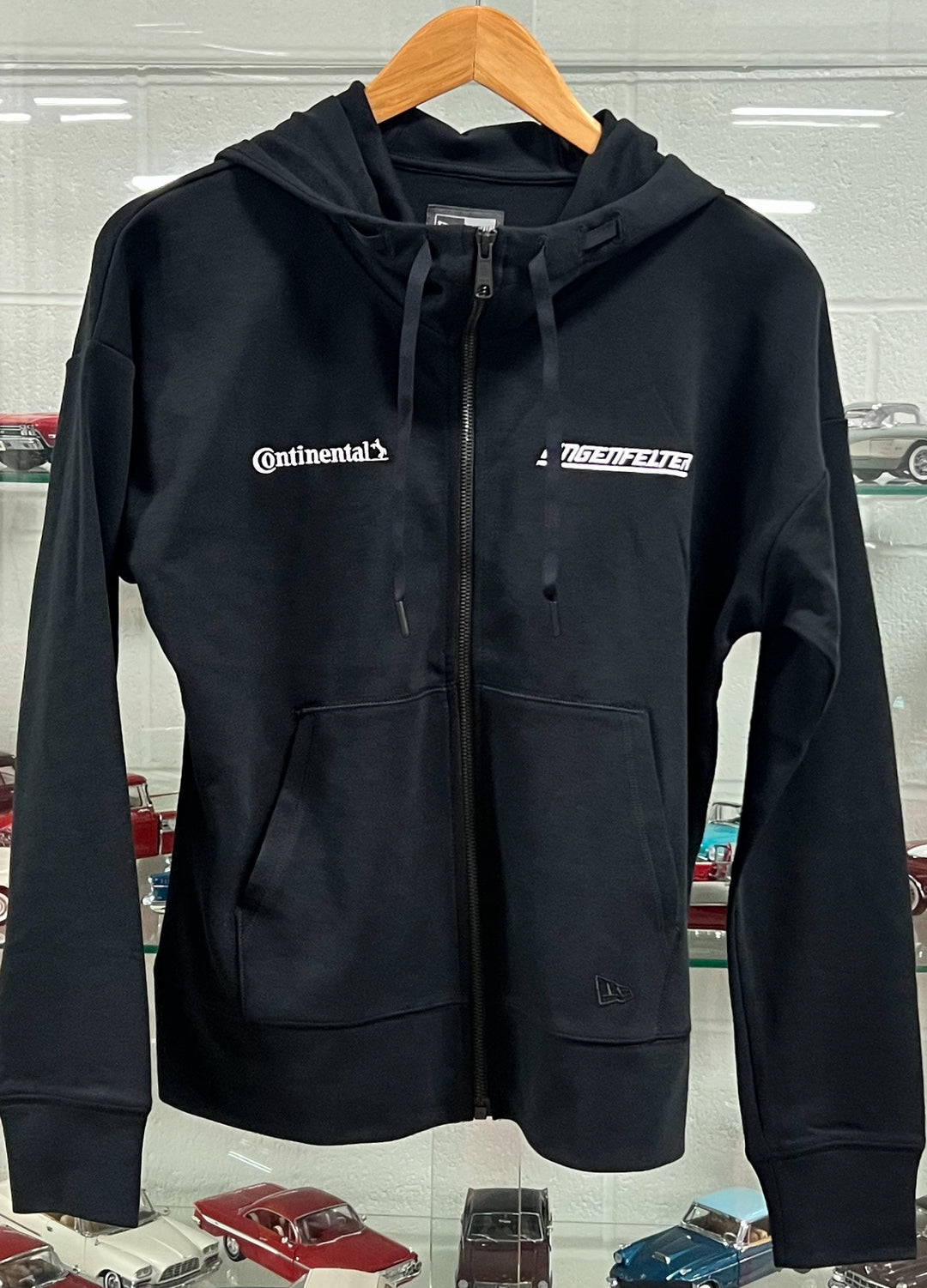 Black hoodie with Continental logo on a hanger against a car-themed background